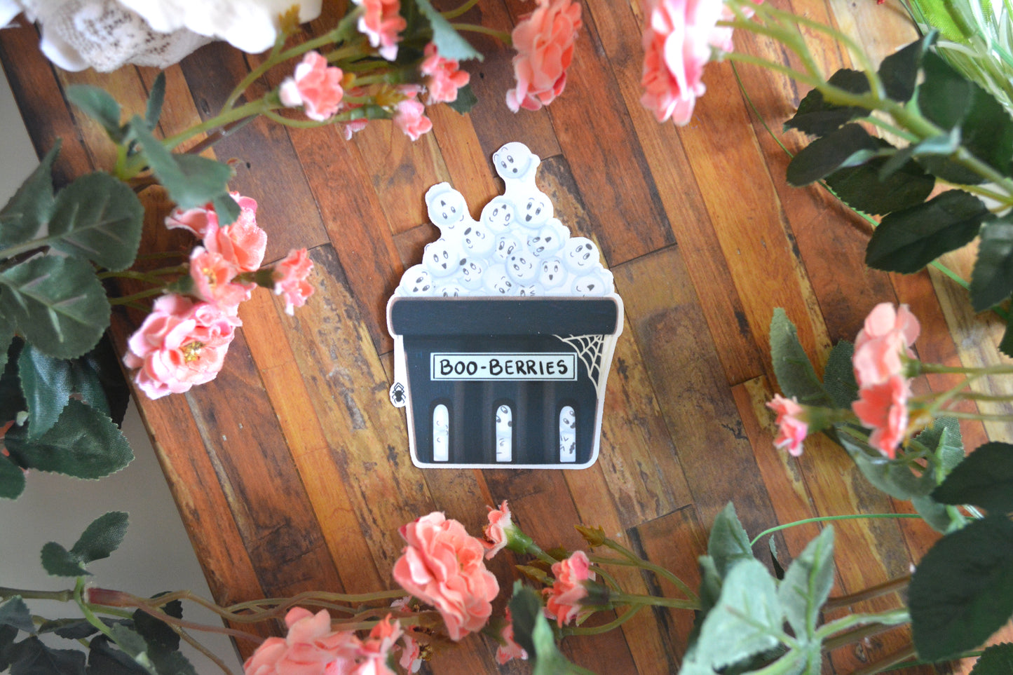 A Halloween sticker of ghostly blueberries in a blue punnet with a spider and spiderweb on it