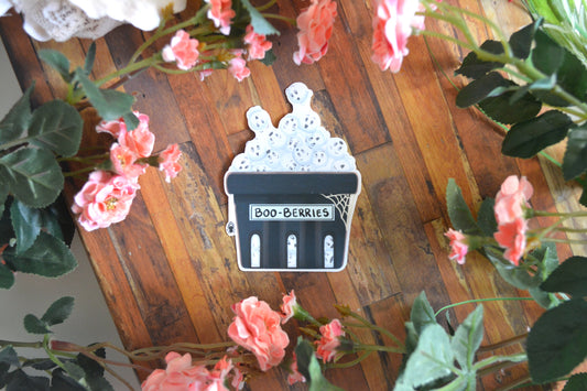 A Halloween sticker of ghostly blueberries in a blue punnet with a spider and spiderweb on it