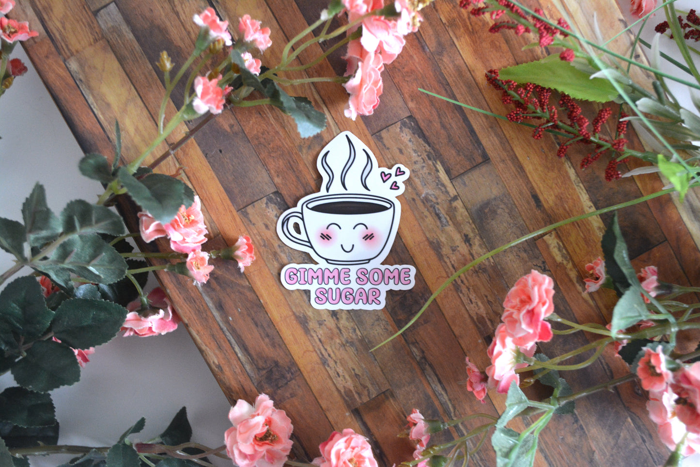 Individual sticker of a coffee and coffee cup illustration with pink hearts and a cute kawaii facial expression and text below it reading "Gimme some sugar."