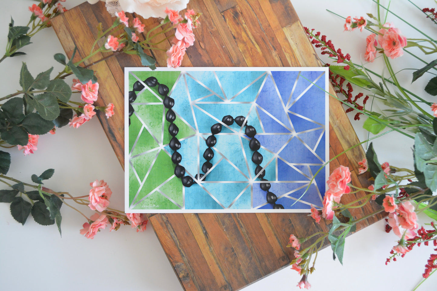 Art print with illustration of a Hawaiian black kukui nut lei intertwined throughout silver lines on a triangular mosaic in shades of green and blue.