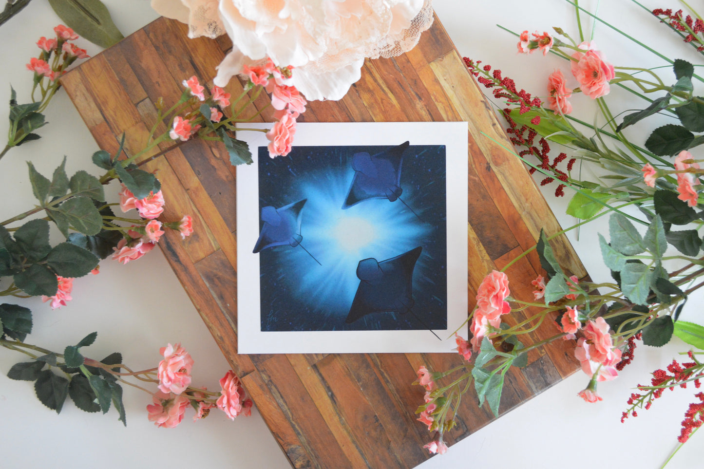 Art print with an illustration of three stingray silhouettes against sunlight streaming into the ocean depths.