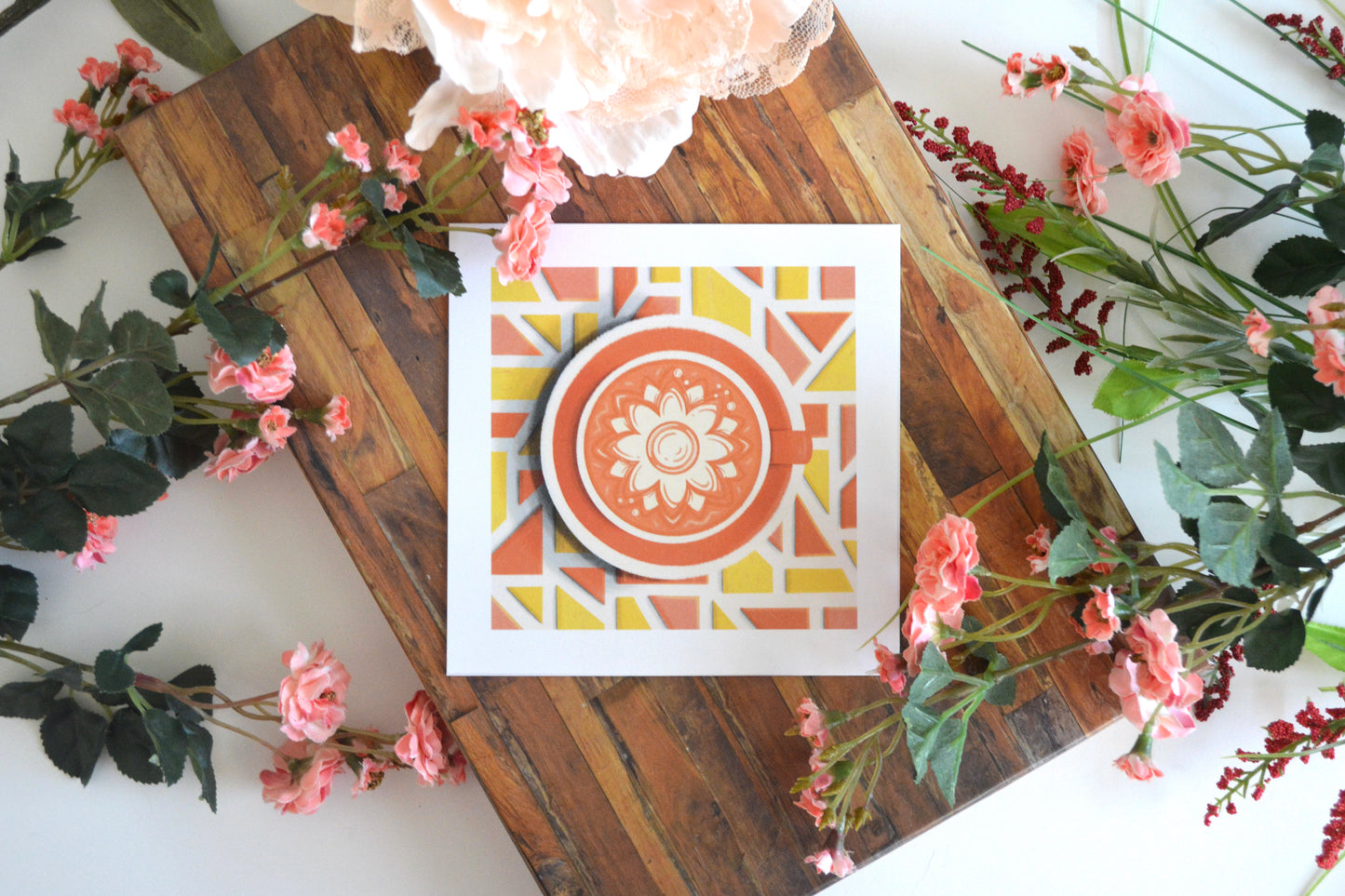 Art print with illustration of sunflower latte art in an orange cup, on an orange plate, on a mosaic tile tabletop in shades of yellow and orange.