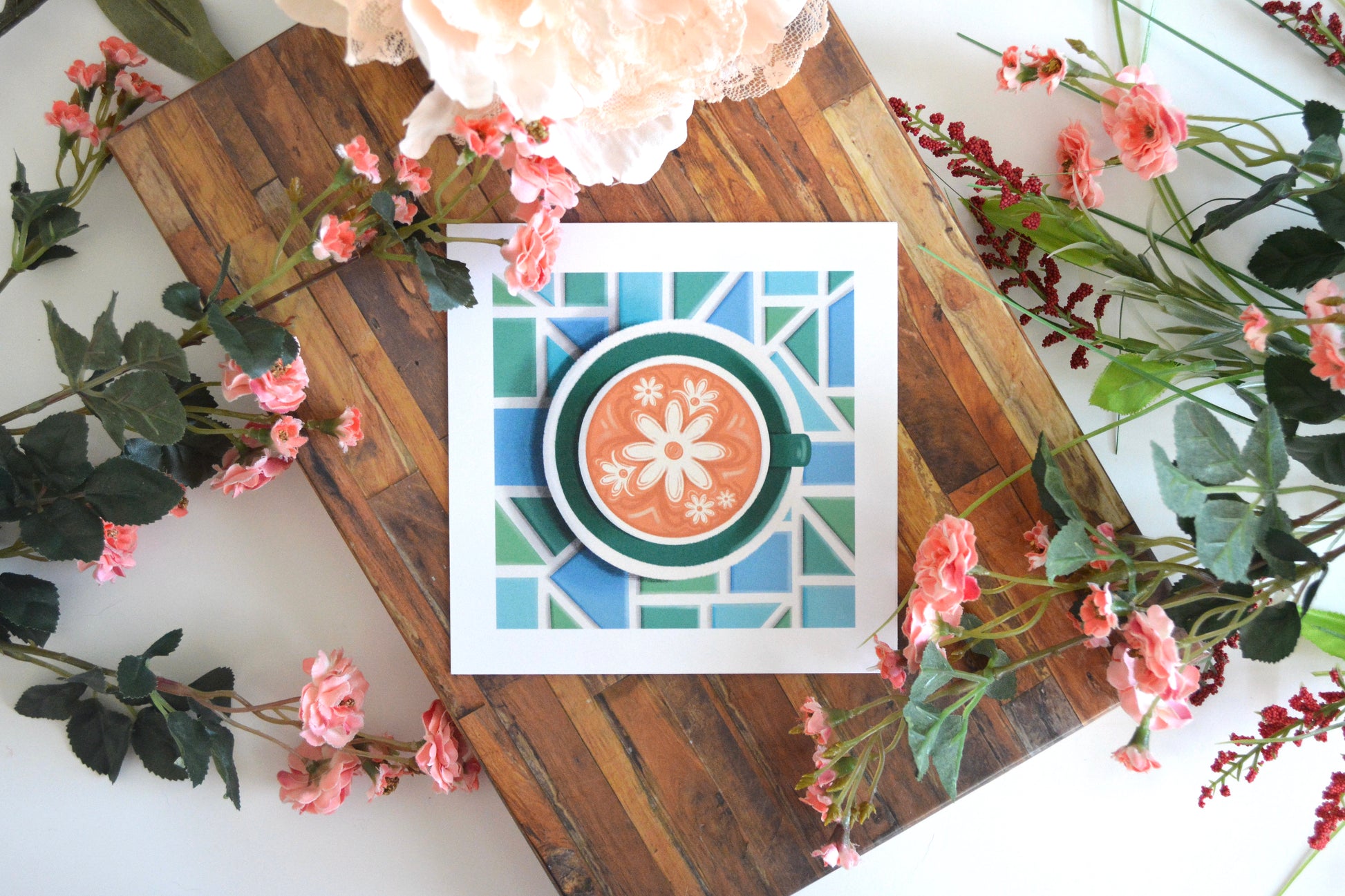 Art print with illustration of daisy latte art in a green cup, on a green plate, on a mosaic tile tabletop in shades of blue and green.
