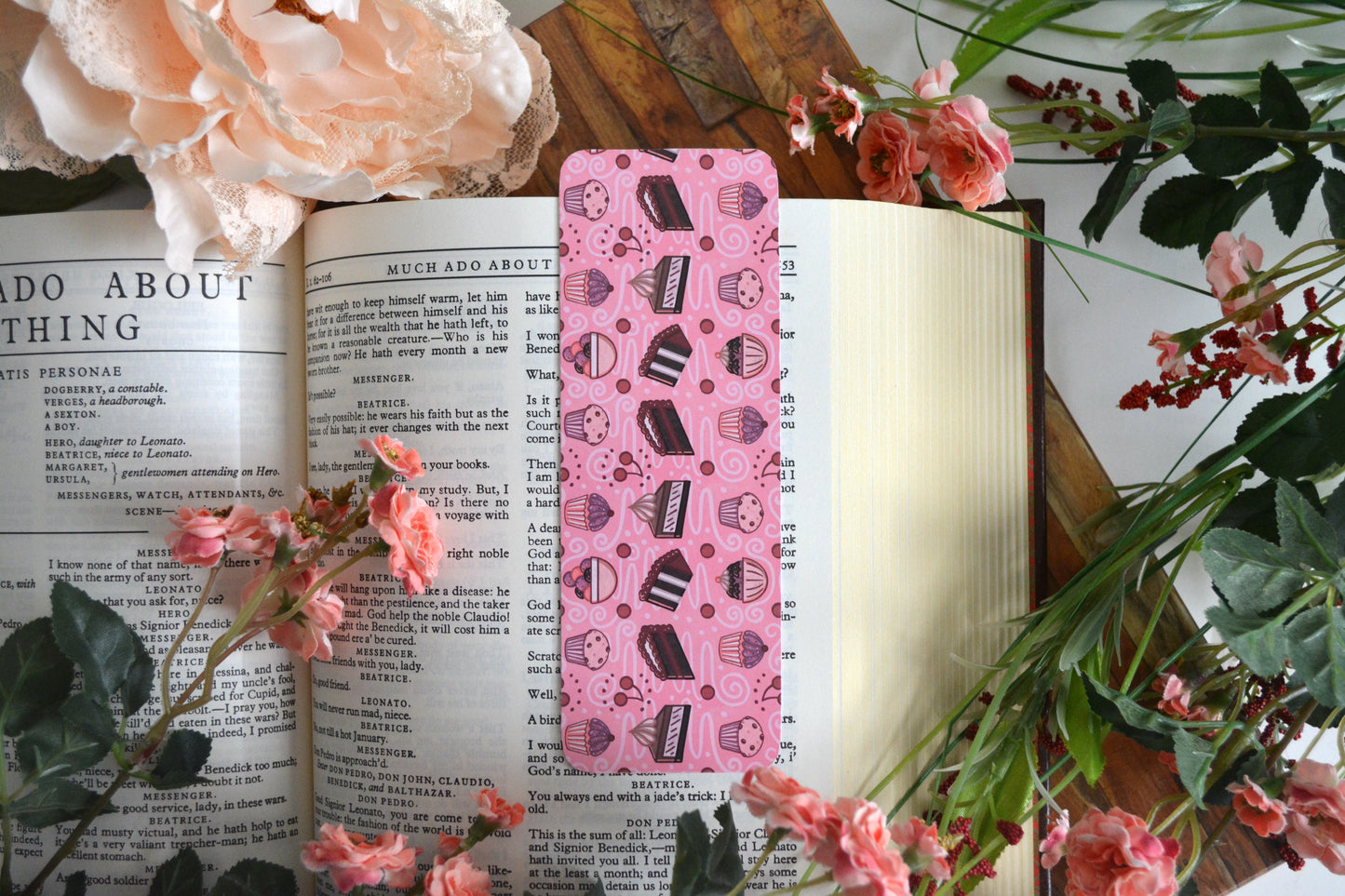Bookmark with illustrations of cupcakes, muffins, cake, pie, ice cream, cherries, and icing drizzle swirls on a light pink background.