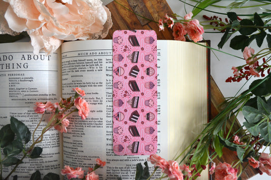 Bookmark with illustrations of cupcakes, muffins, cake, pie, ice cream, cherries, and icing drizzle swirls on a light pink background.